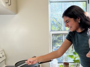 a Hindi language student smiling and laughing while standing in front of a stove tending to a puri frying in a pan with oil.