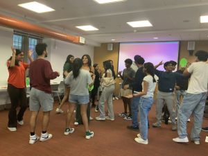 A group of about 15 Hindi 203 students gathered in a classroom preparing a street play. Many are smiling and/or gesticulating as the interact with each other.